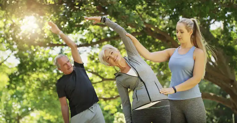 A personal trainer guding two seniors in a workout at the park