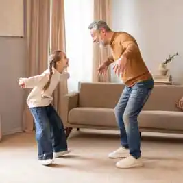 Active senior man playing with granddaughter at home, showing strength and independence through movement